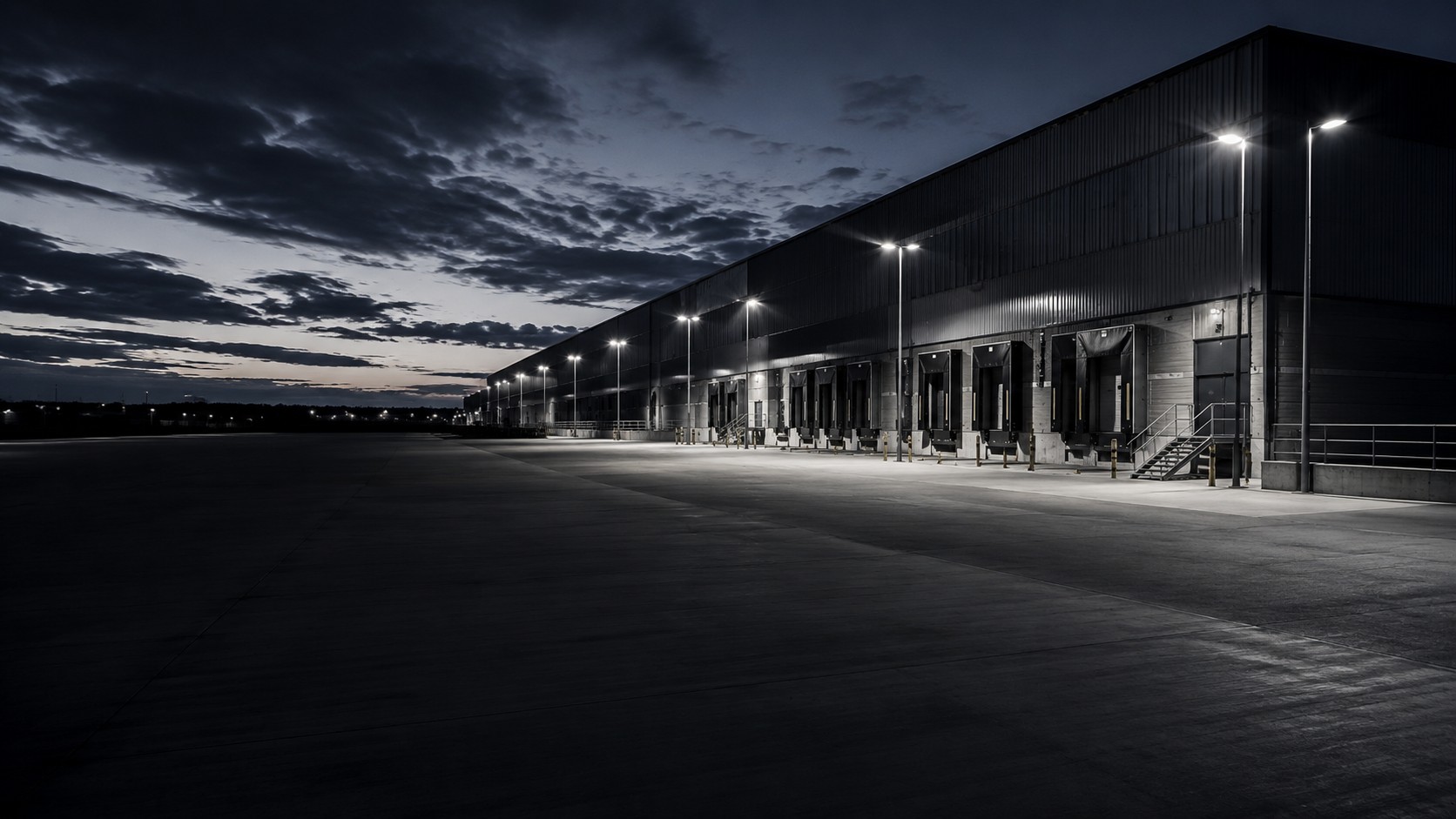 Exterior of a large operational facility at dusk with its service yard lit by pole lights