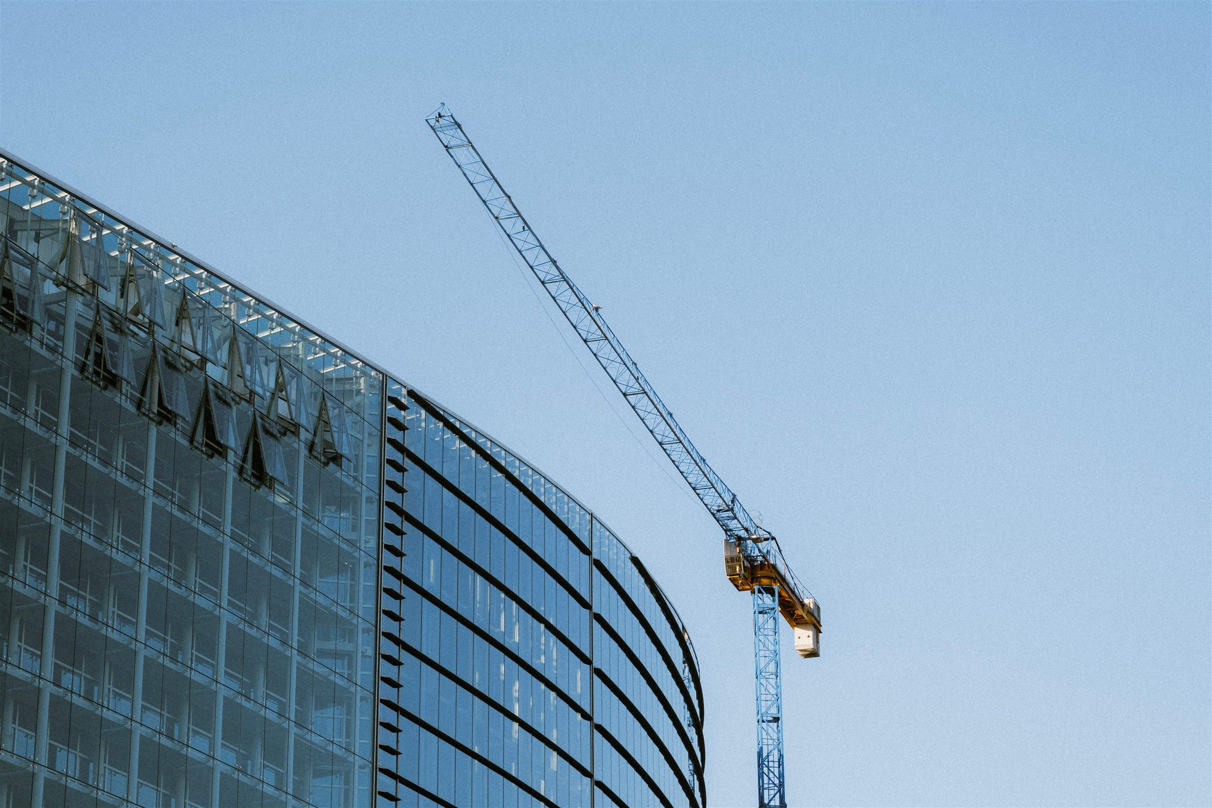 Glass office tower under construction beside a tower crane, set against open sky