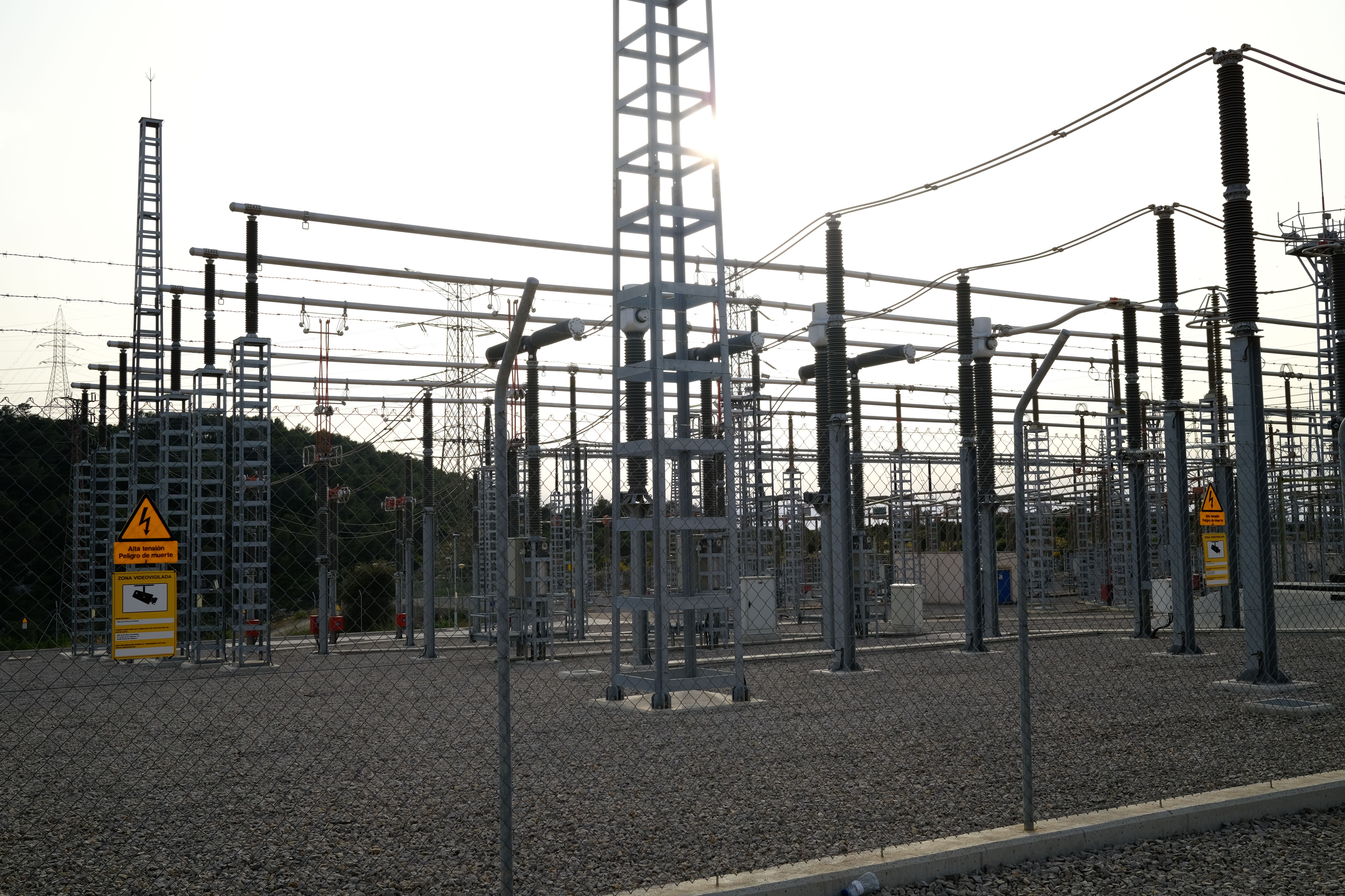 High-voltage electrical substation yard with transformers and switchgear behind a security fence